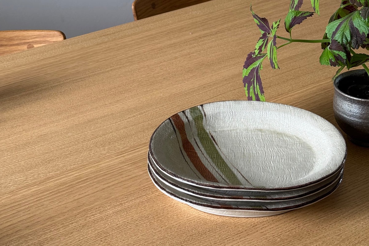 Stack of vintage Japanese stoneware plates with stripes on a light wooden dining table