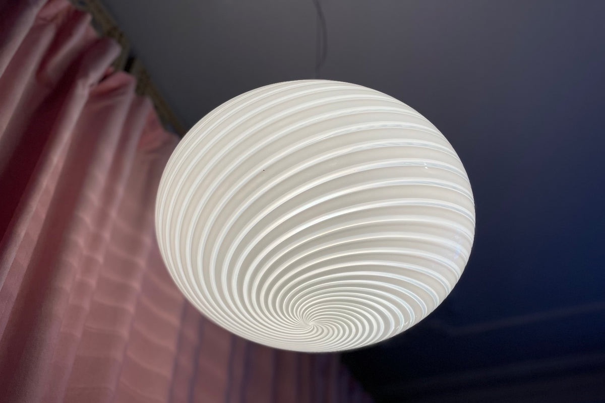 Lit white vintage Murano pendant with a swirl pattern seen from below in front of a pink curtain