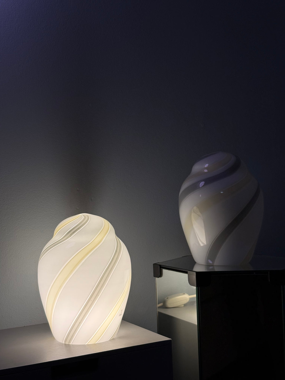 Tændt vintage Murano bordlampe helt i hvidt glas med gul og grå swirl på en spejlsokkel