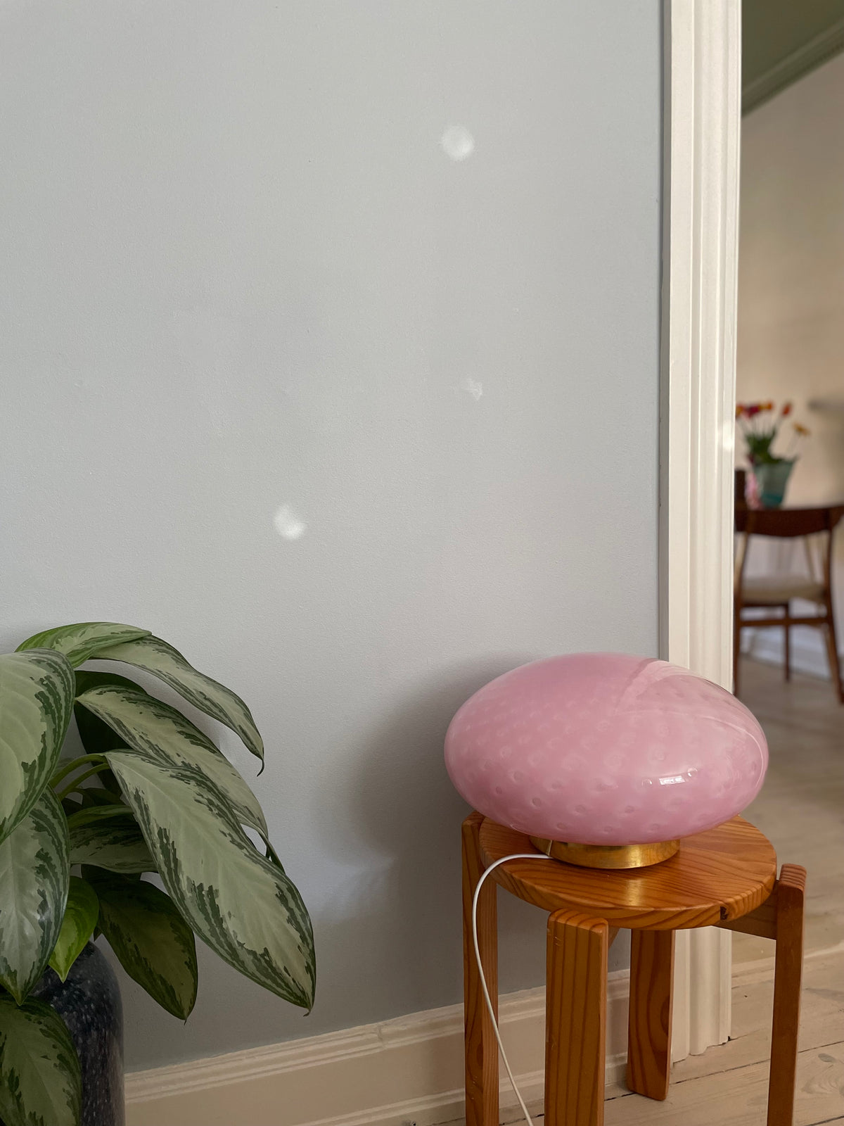 Lyserød plettet vintage Murano lampe på en taburet i træ ved siden af en plante