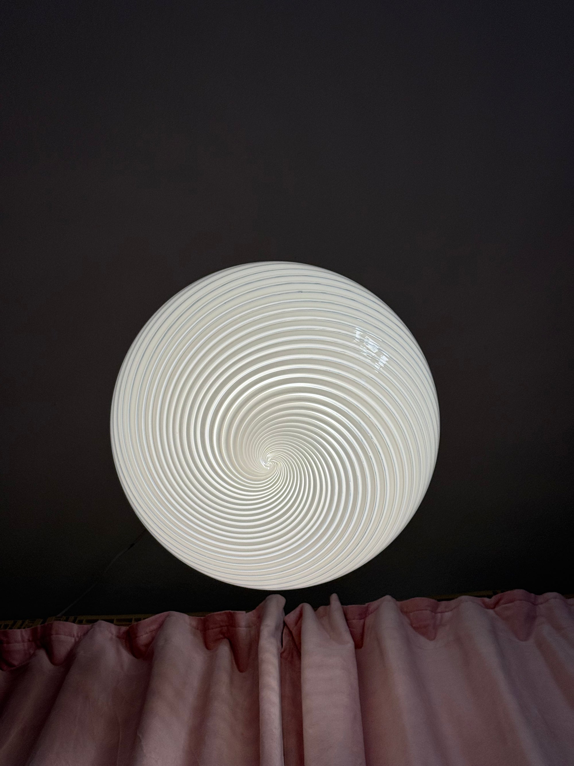 Tændt Murano plafond med swirl-mønster monteret over et lyserødt gardin